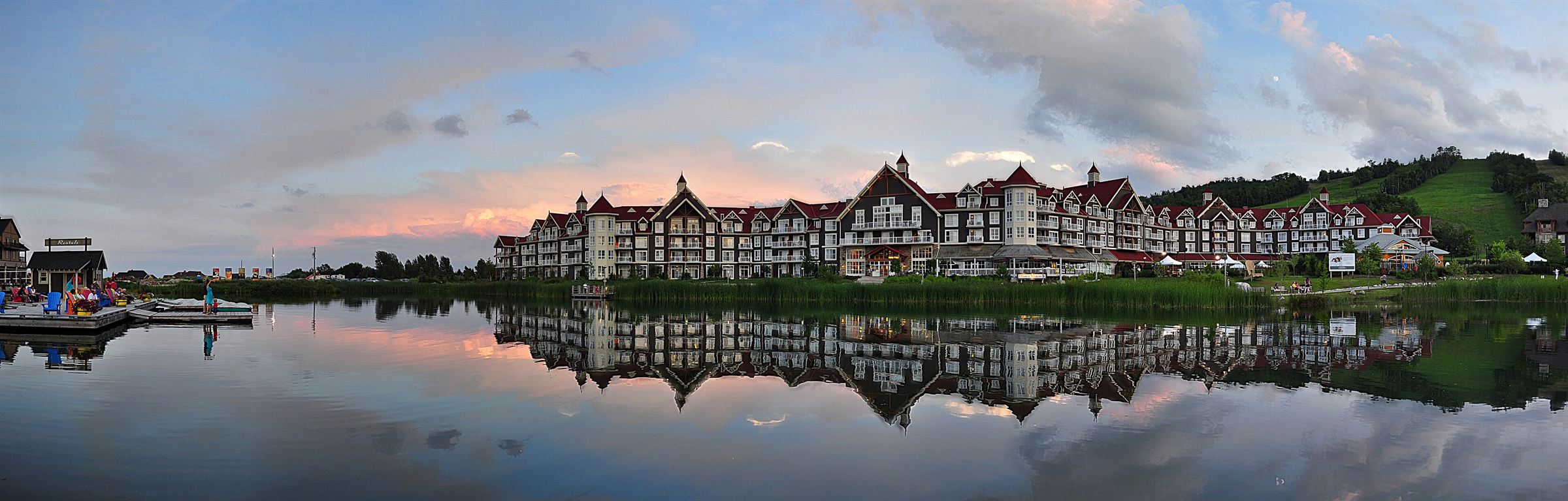 A pink summer sunset over the Mill Pond, with the Village lodges and green ski hill mirrored in the water