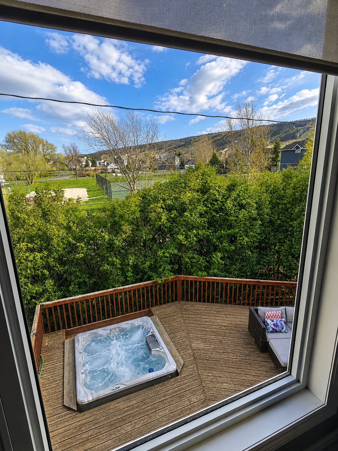 View down from a loft window to the hot tub on the deck, with the green ski hill beyond the cedars