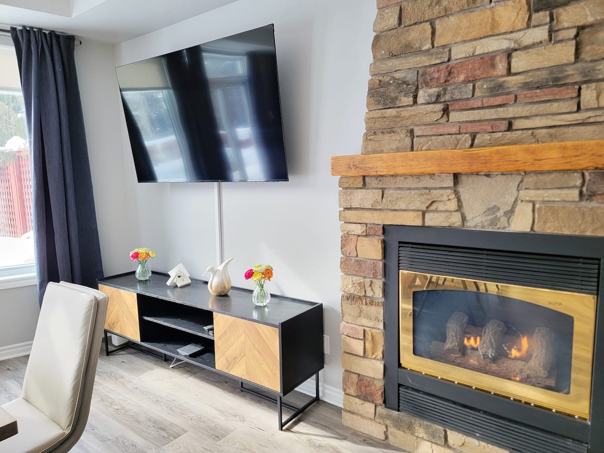 Stacked-stone fireplace with a wooden mantel, lit, beside a wall-mounted TV