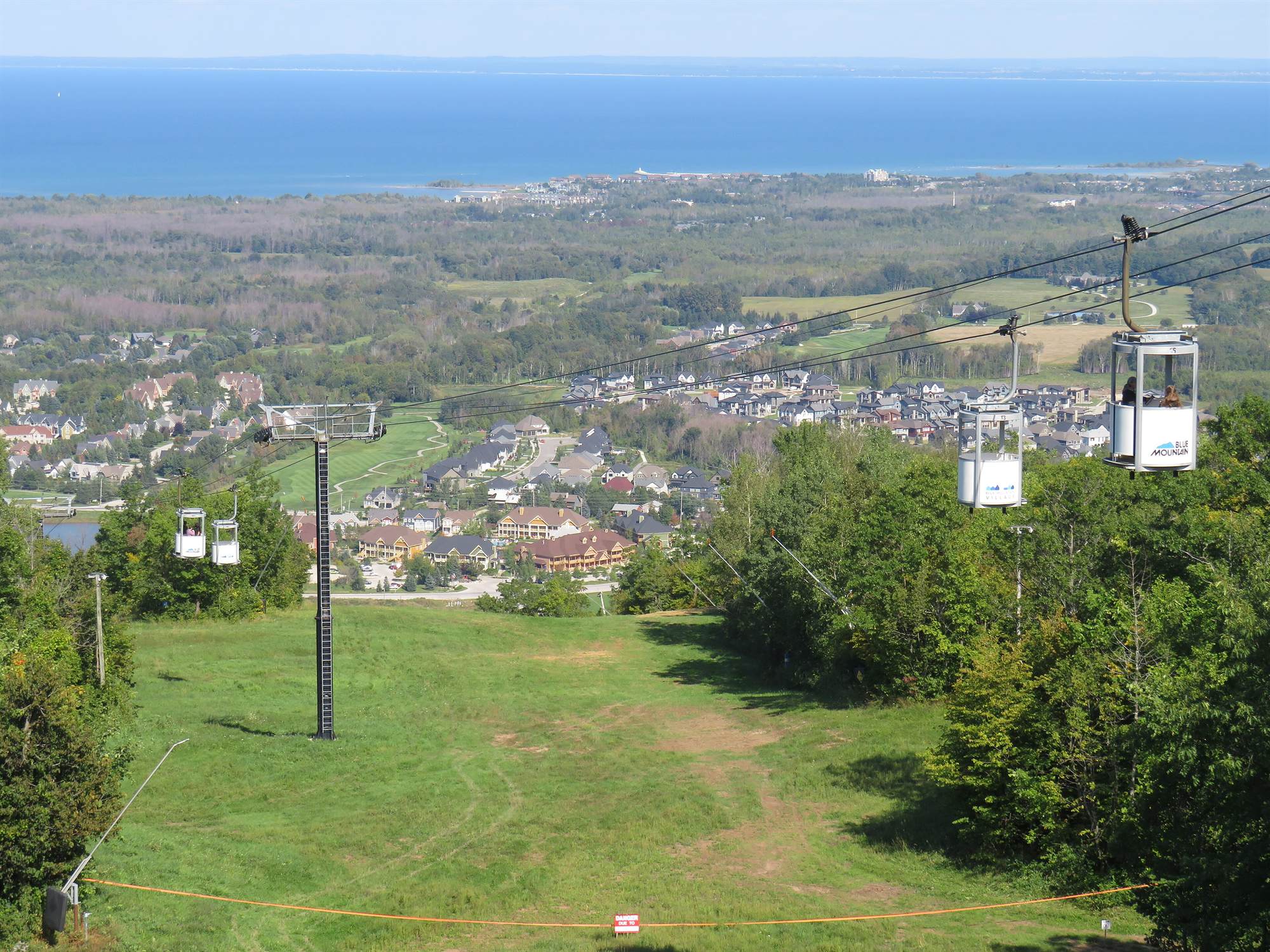 Gondola cabins above a green ski run, looking down over the Village, farmland and Georgian Bay